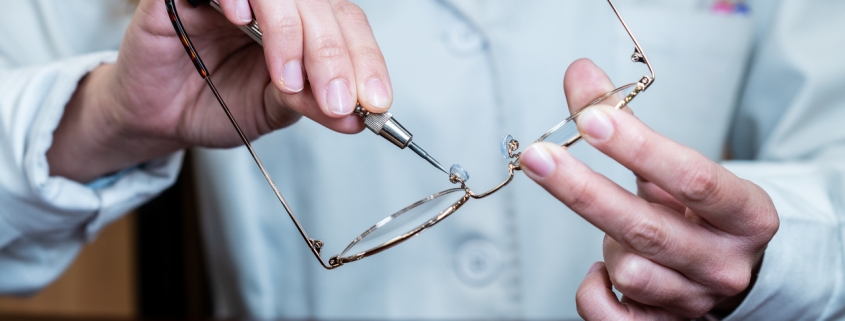 Female optician repairing and fixing eye glasses with screwdriver. Hands holding a mini screwdriver, maintenance and cares service. Frontal view